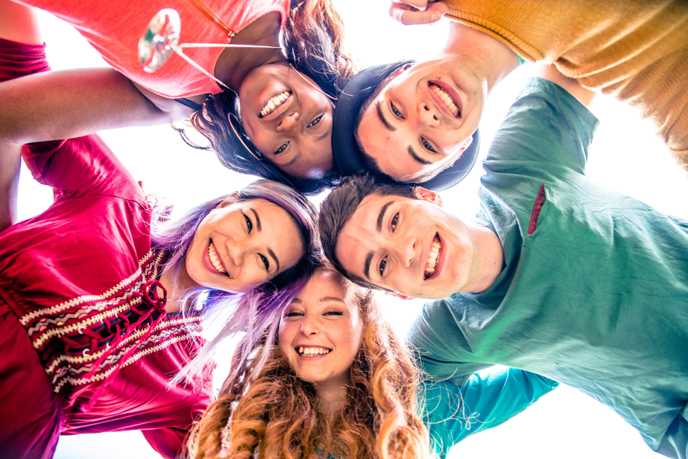 Vijf jongeren die elkaar omhelzen in een cirkel starend naar de camera.